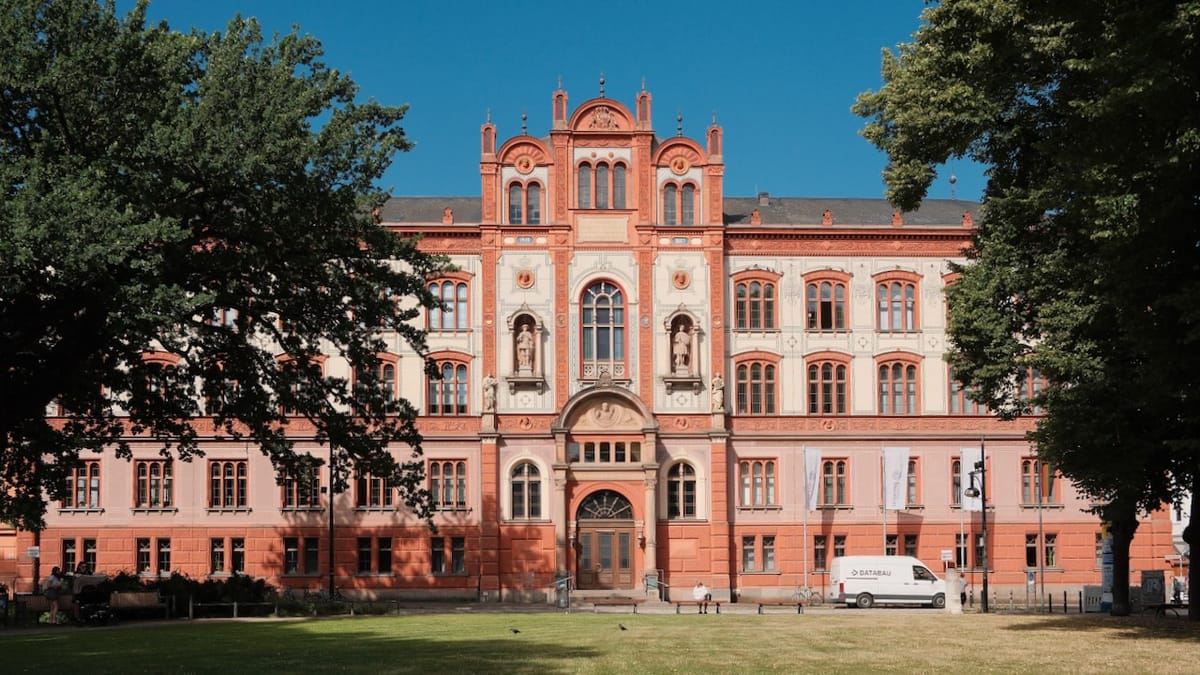Das Universitäts-Hauptgebäude Rostock im warmen Sommerlicht, umgeben von Bäumen und blauem Himmel – ein Beispiel für die weiche norddeutsche Lichtstimmung.